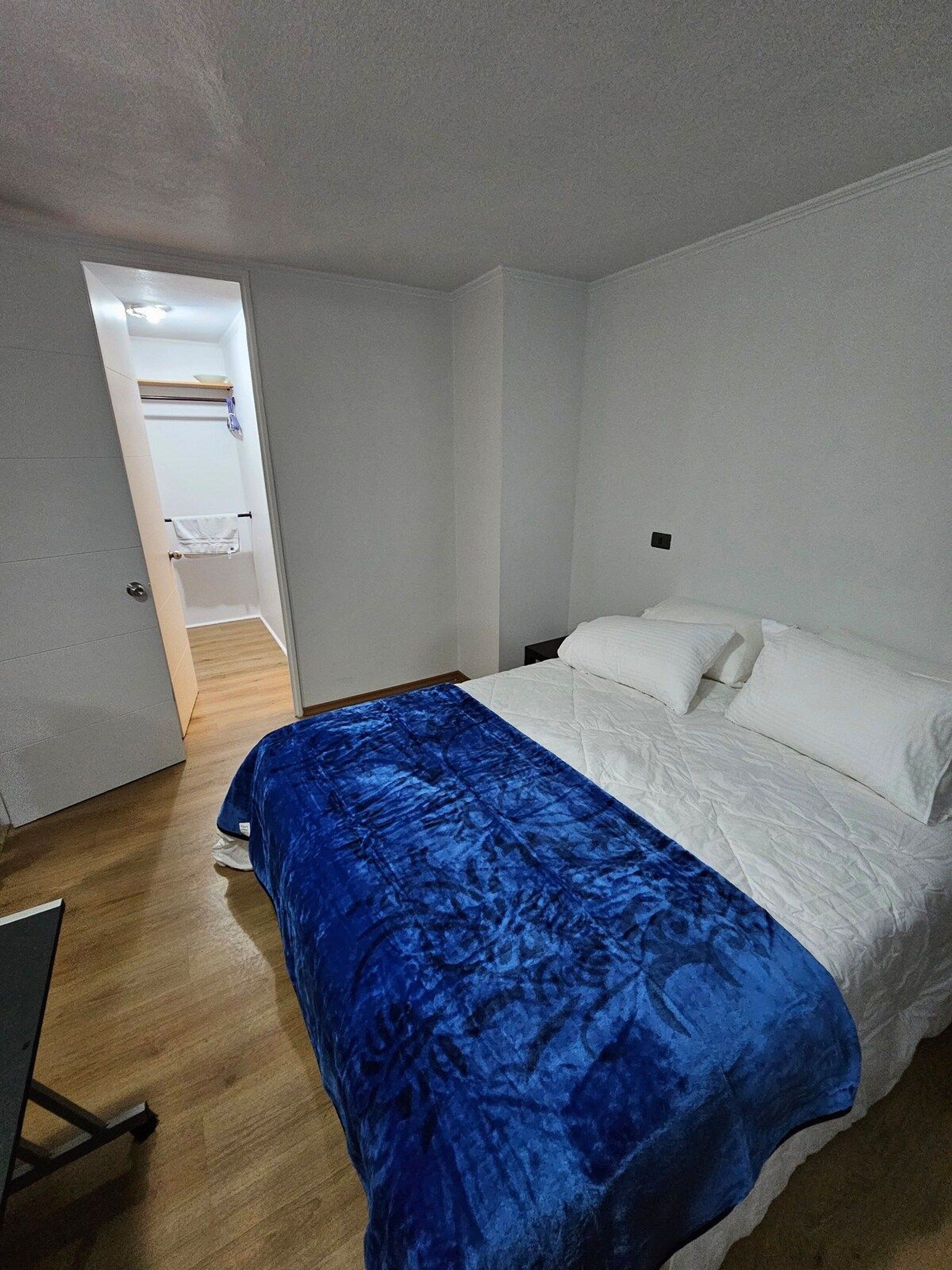 A bedroom with a bed, a blue blanket, and a wooden floor.