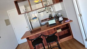 A compact kitchen with a wooden countertop, two black bar stools, and a built-in shelf above the counter. - Dardigniac (Santiago)