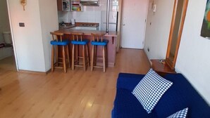 A compact living space with a kitchenette, a blue sofa with checkered pillows, and a wooden floor. - Dardigniac (Santiago)