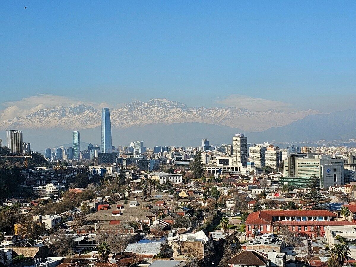 A cityscape with a prominent skyscraper and a mountain range in the background.