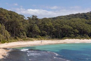 A beach with clear turquoise waters, a sandy shore, and dense forested hills in the background.