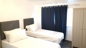 Una habitación con dos camas, un armario y un ventanal con cortinas.