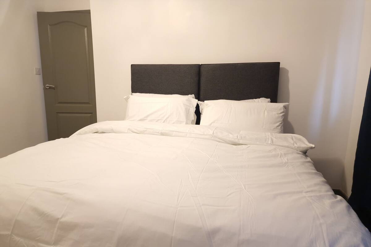 A bed with white bedding and a dark headboard in a room with white walls.