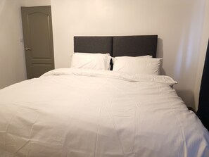 Una cama con ropa de cama blanca y un cabecero oscuro en una habitación con paredes blancas.