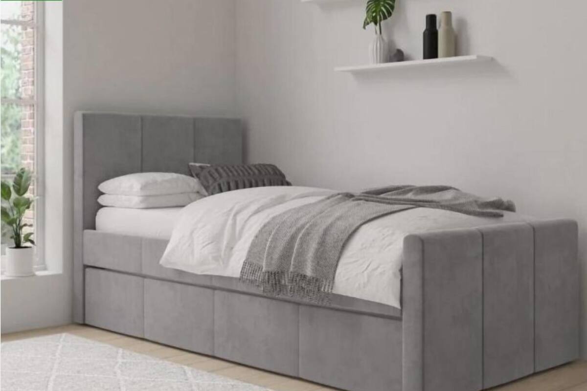 A modern bedroom with a grey upholstered bed, white bedding, and a small shelf with decorative items.