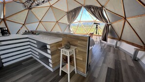 A modern, geometric-themed interior with a central bar area, a wooden stool with a vase, and a large window offering a view of the outdoors. - Santerra, Guadalupe Valley (Valle de Guadalupe)