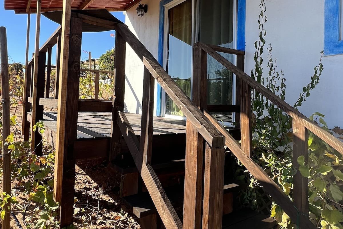 Een houten trap in landelijke stijl leidt naar een overdekte veranda met een rood dak.