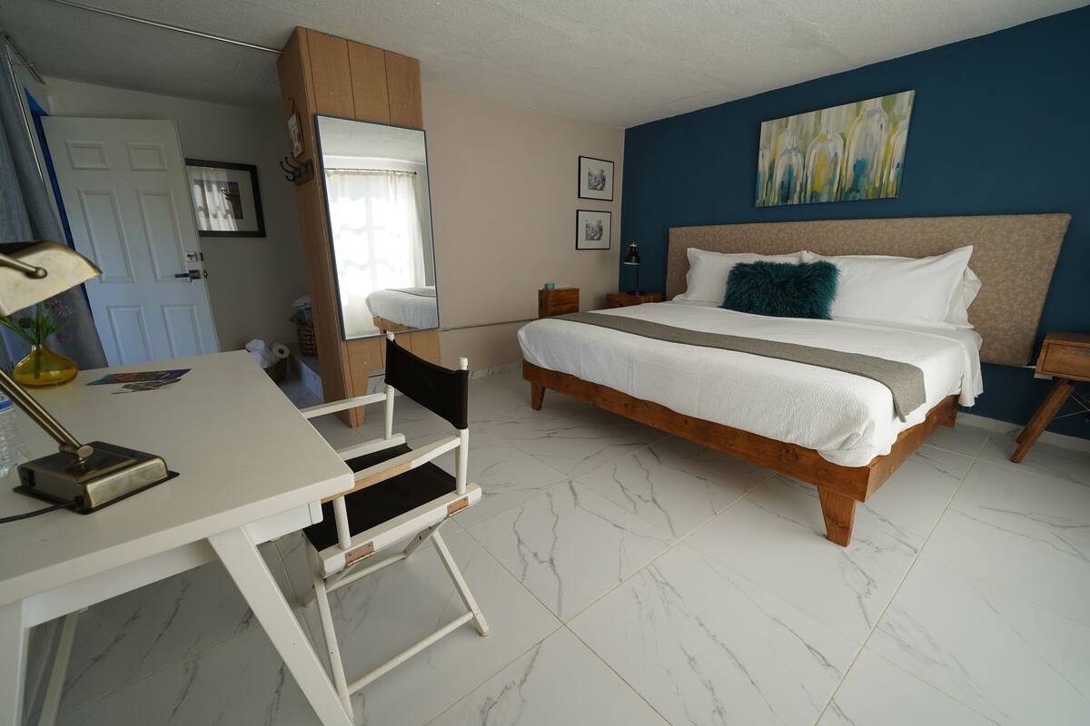 Een slaapkamer met een bed, een bureau, een stoel, een spiegel en een deur.