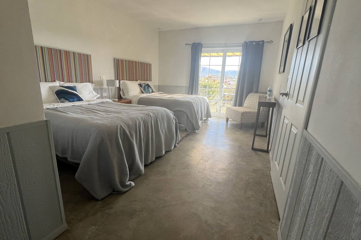 Een hotelkamer met twee bedden, een kleine tafel, een stoel en een raam met uitzicht op de omgeving.