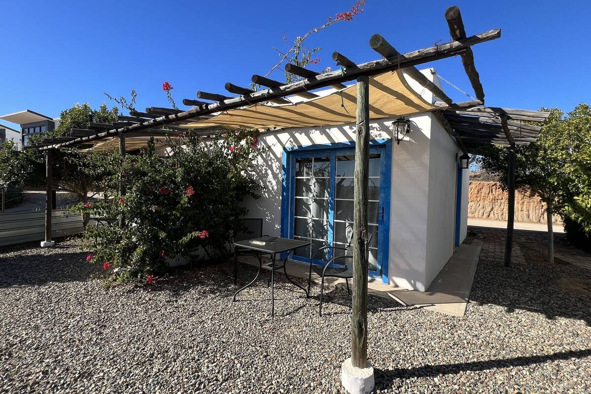 Een overdekt terras met een pergola, een tafel en stoelen, omgeven door grind en beplanting.