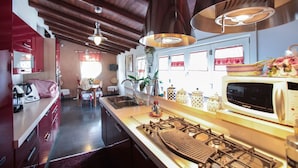 Una cocina moderna con estufa a gas, pileta de acero inoxidable y microondas. Cuenta con alacenas de madera y una cubierta de encimera roja.