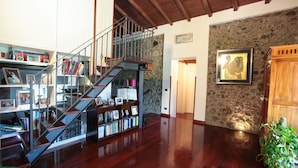 Un amplio salón con una escalera de madera, una pared de piedra y una estantería llena de libros.