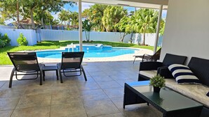 Un patio techado con piscina, mobiliario exterior y vista al jardín.