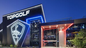 Un edificio moderno con un llamativo letrero de 'TOPGOLF' y un símbolo de golf neón.