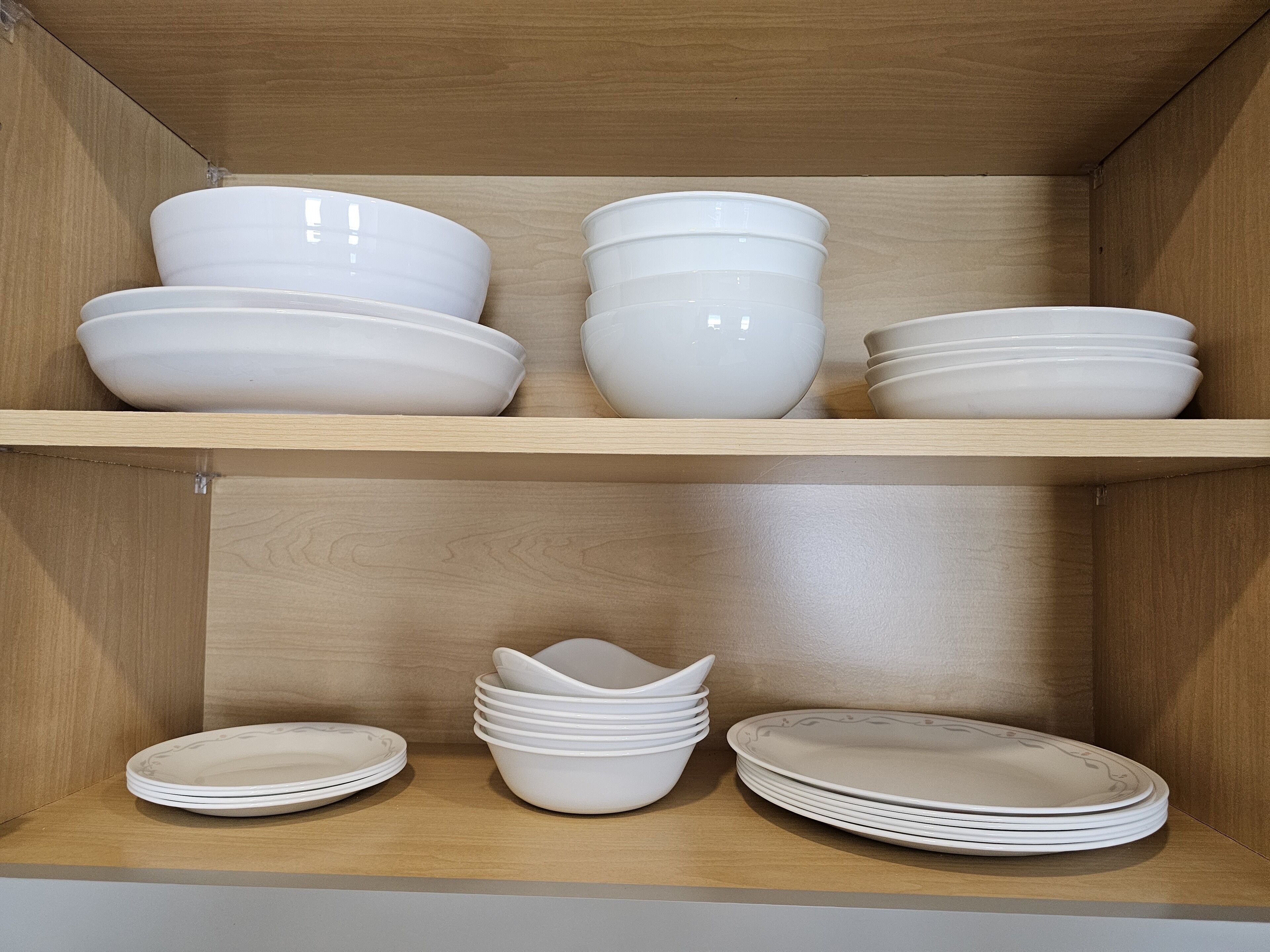 A wooden cabinet with two shelves, each holding stacks of white bowls and plates.
