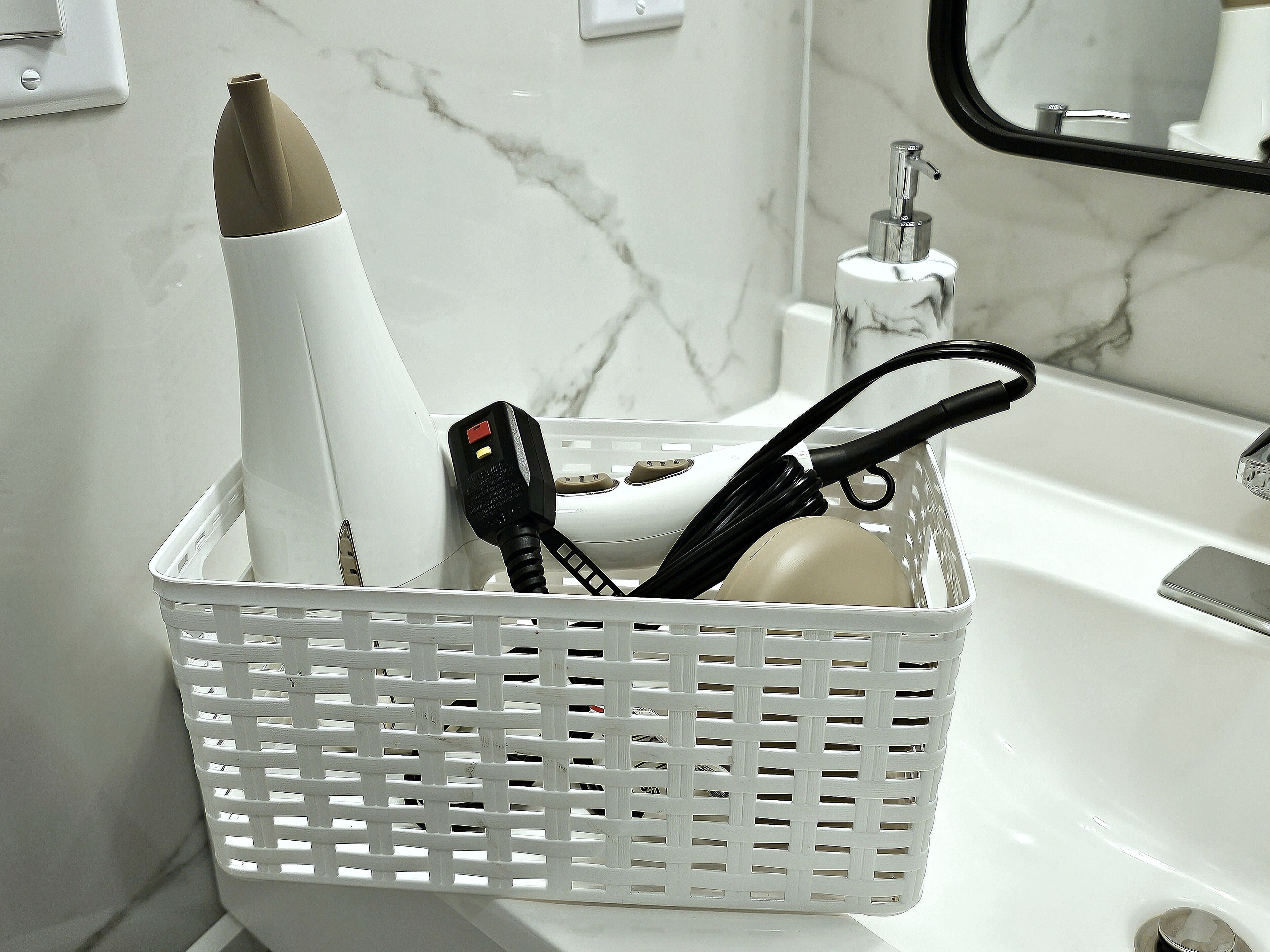 Un bagno con un lavabo in marmo bianco, un cesto bianco contenente un asciugacapelli, una spazzola per capelli nera e una bottiglia bianca.