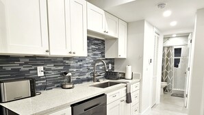 A modern kitchen with white cabinets, a built-in microwave, a coffee maker, and a dishwasher.