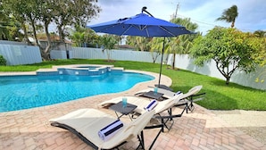 A swimming pool with lounge chairs and an umbrella.