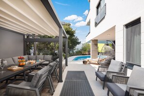 An outdoor patio with a dining table, chairs, a pool, and a hanging chair.