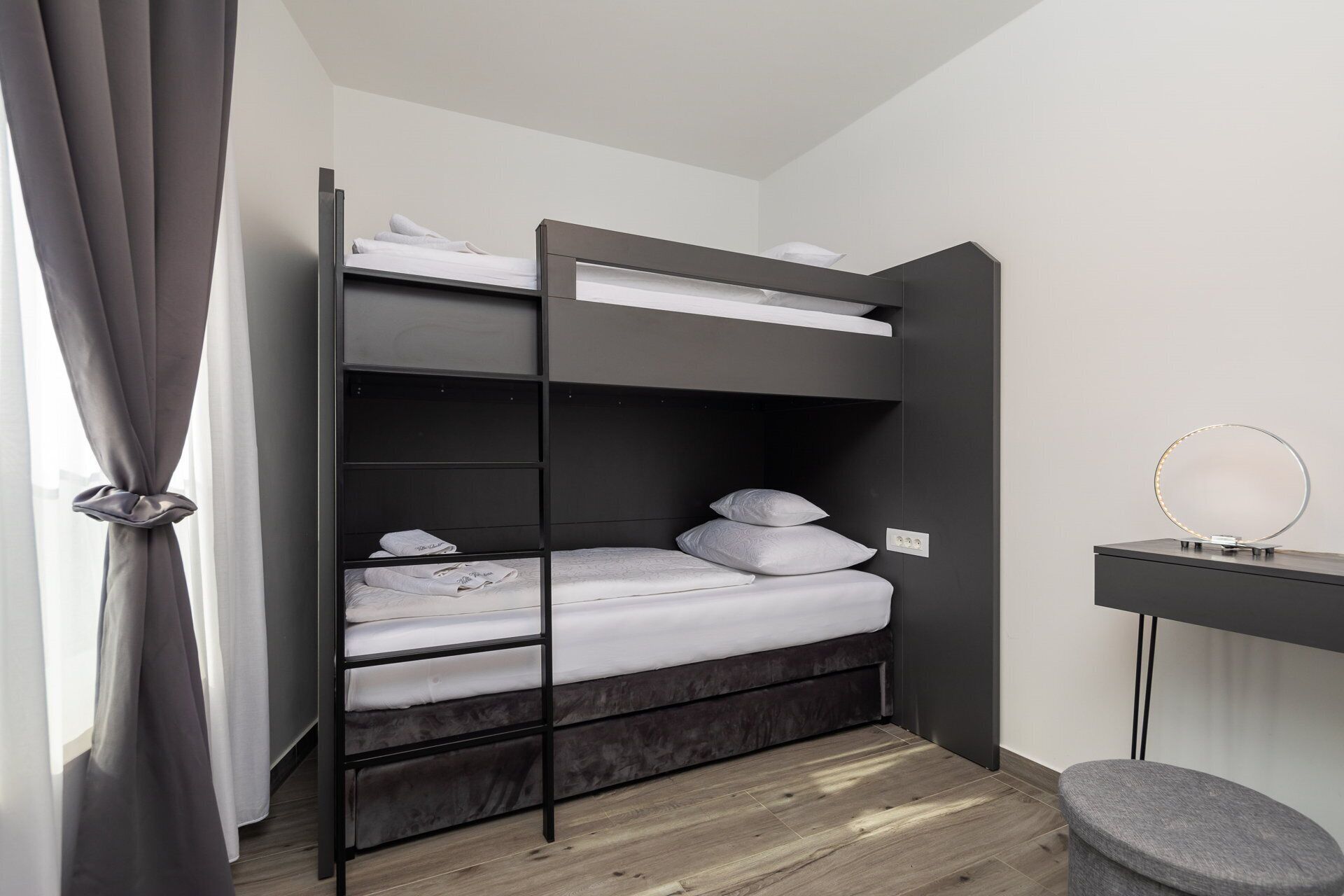 A bunk bed with a desk and a mirror, a grey curtain, and a small stool.