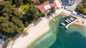 Vista aérea de uma área costeira com praia arenosa, águas turquesa cristalinas e vários barcos ancorados perto da costa.