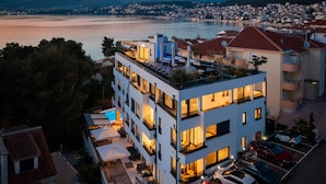 Um hotel moderno com vários andares, varandas, área de estar ao ar livre e vista para um lago e o horizonte urbano ao entardecer.