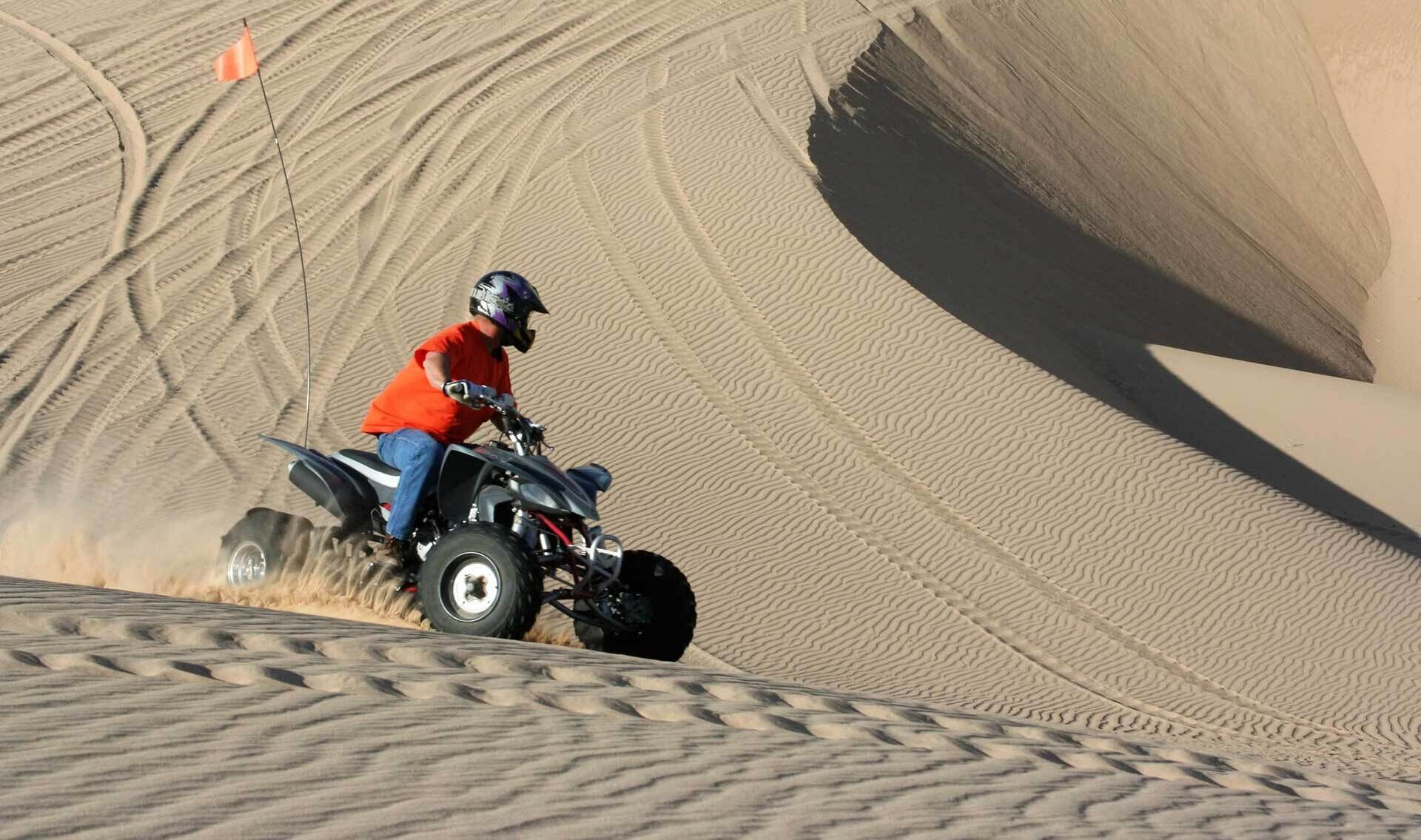 A person riding a quad bike on a sandy dune.
