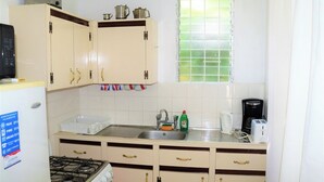 A compact kitchen with a gas stove, a sink, and a window with a green-tinted glass.