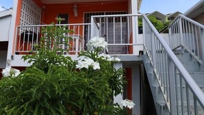 A multi-story building with a red and white facade, a balcony with white railings, and a staircase with metal railings.