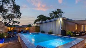 Une piscine avec une terrasse en bois, des chaises longues et un espace salon abrité.
