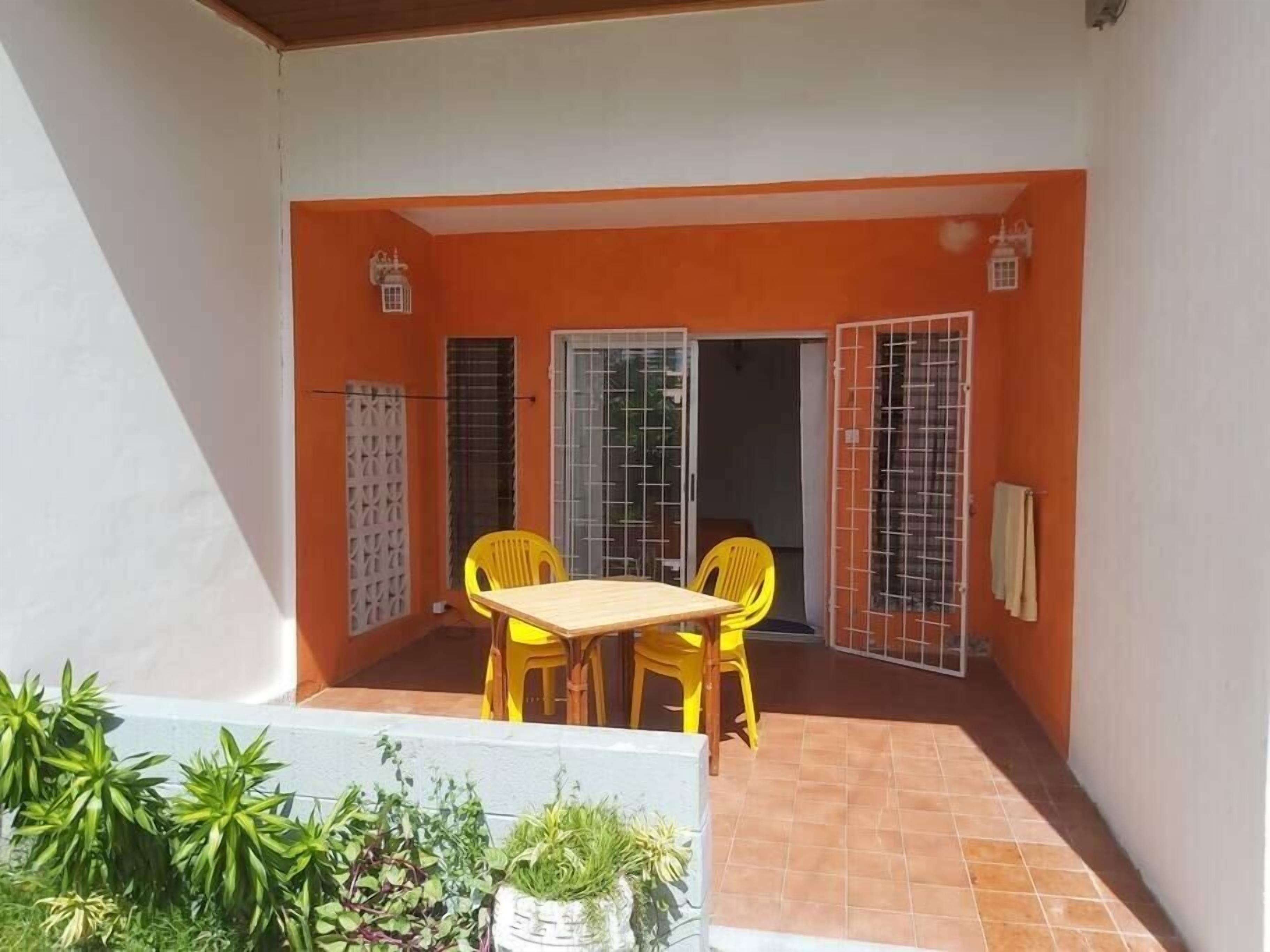 Un piccolo patio con un tavolo di legno e sedie gialle, circondato da pareti arancioni e un pavimento piastrellato.
