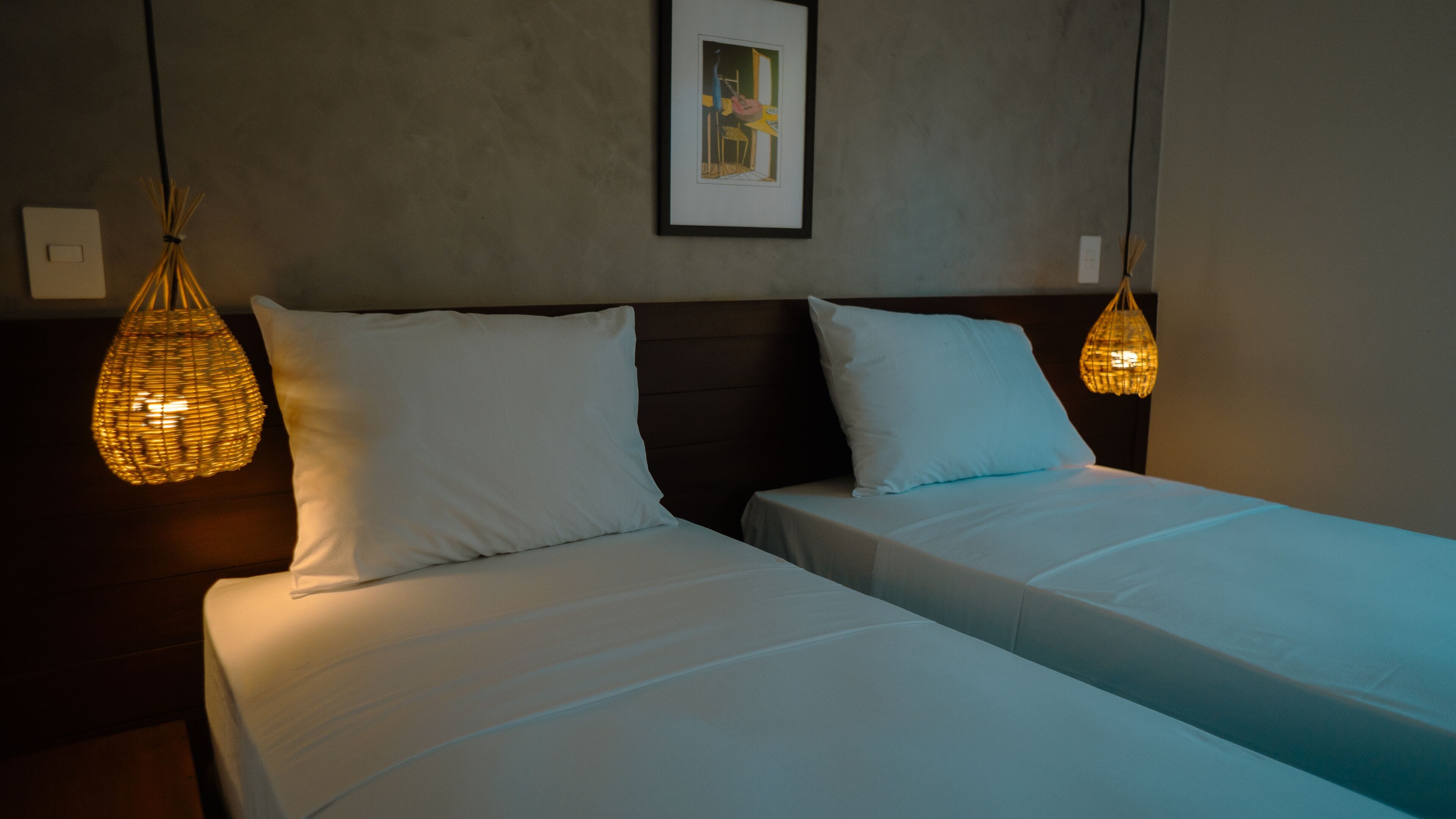 Ein Hotelzimmer mit zwei Betten, einem gerahmten Bild an der Wand und zwei Pendelleuchten.