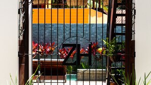 A gated entrance with a brick pathway leading to a building with a yellow and orange facade. - Zenhousepipa (Tibau do Sul)