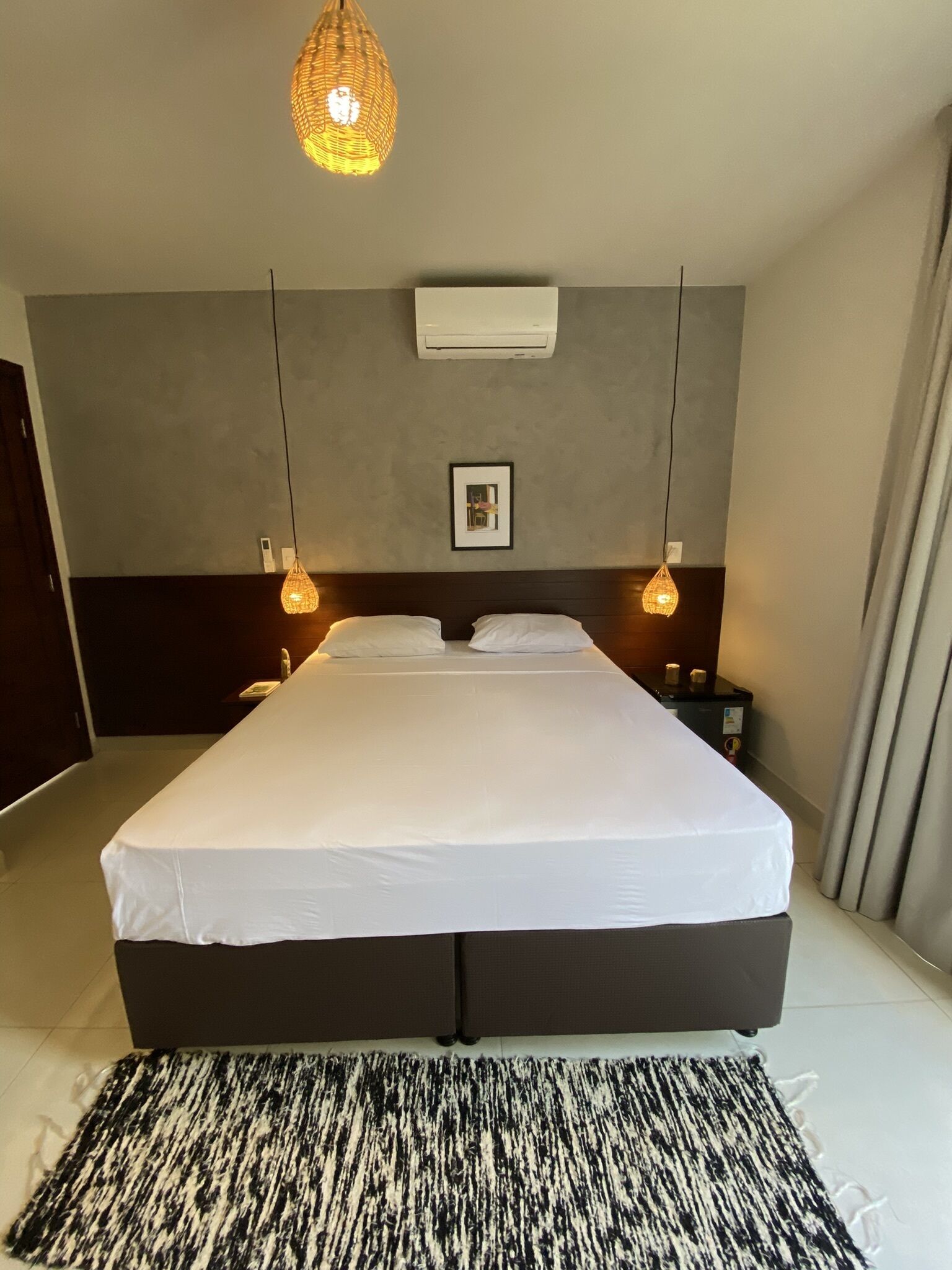 Habitación de hotel con una cama grande, dos lámparas de noche, aire acondicionado y un cuadro en la pared.
