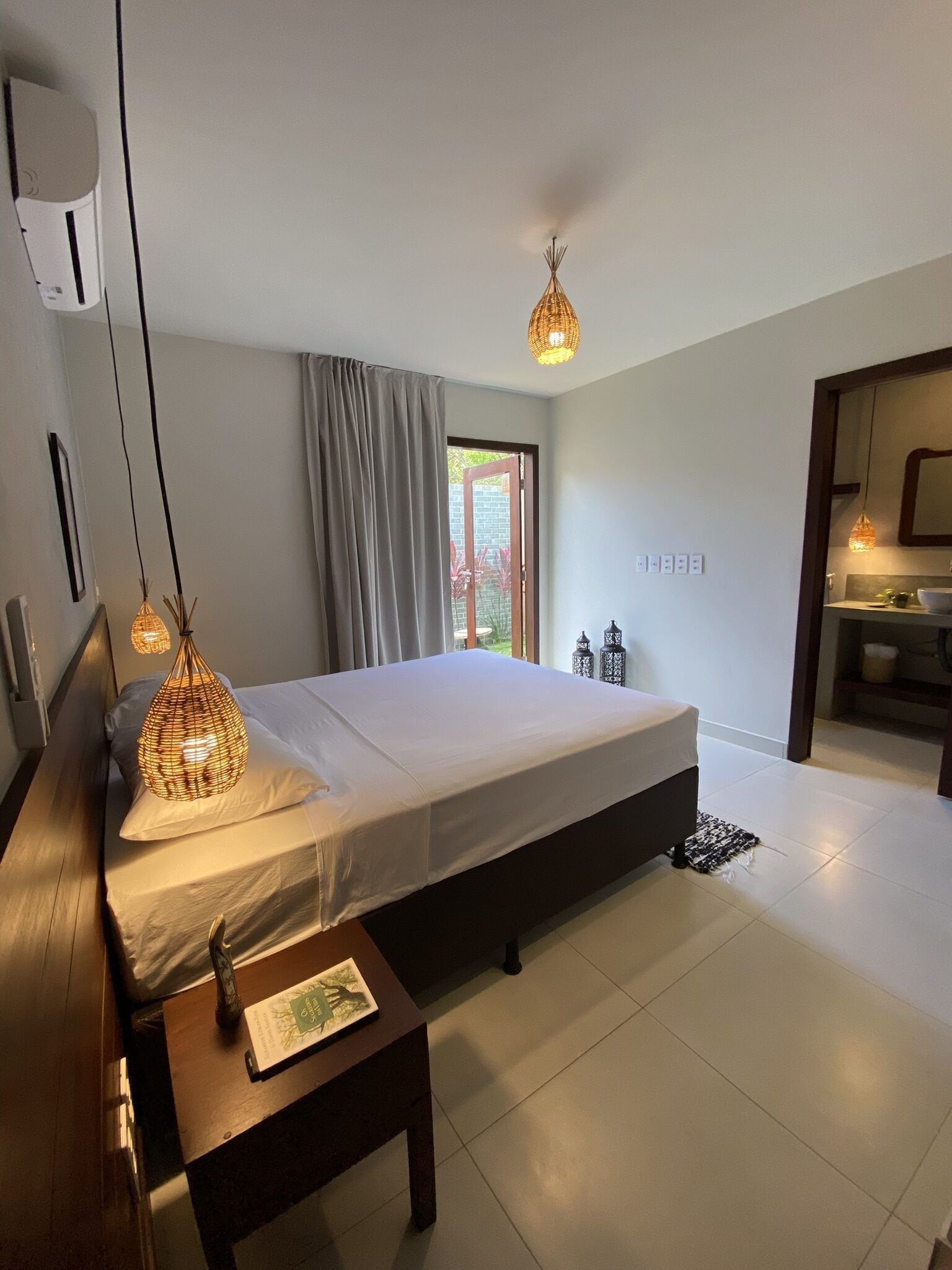 A modern bedroom with a large bed, bedside lamps, a small table, and a view of the outdoors.