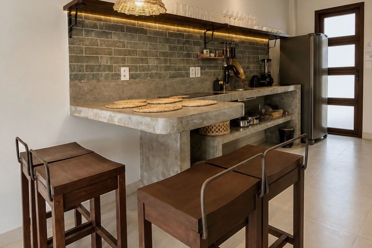 A modern kitchen with a central island, bar stools, and a hanging light fixture.