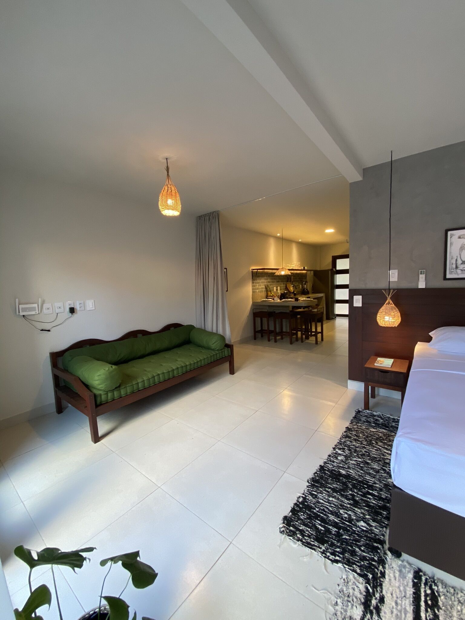 A modern hotel room with a green sofa, a dining area, and a bed with a black and white rug.