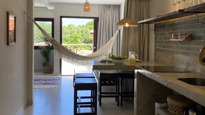 A modern kitchen with a dining area, a hammock, and a view of greenery. - Zenhousepipa (Tibau do Sul)
