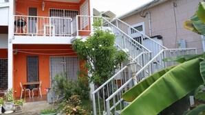 A two-story building with a balcony, a staircase, and a small garden area. - Ocean View Apartment B with AC (Bridgetown)