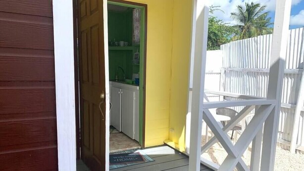 A wooden door leading to a kitchen with white cabinets and a green wall. - Dover Beach Tiny House w kitchen (Oistins)