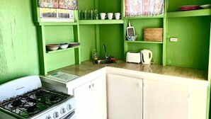 A kitchen with green walls, a white stove, and various kitchen items. - Dover Beach Tiny House w kitchen (Oistins)