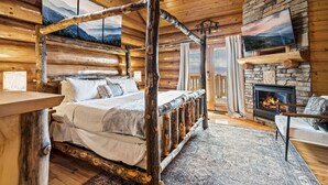 Een slaapkamer in een blokhut met een hemelbed, een stenen openhaard en een grote televisie aan de muur bevestigd.
