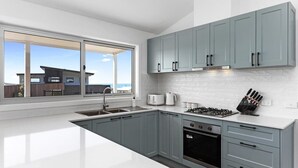 A modern kitchen with grey cabinets, a white countertop, a built-in oven, and a window overlooking a residential area. - Apollo Bay Getaway (Apollo Bay)