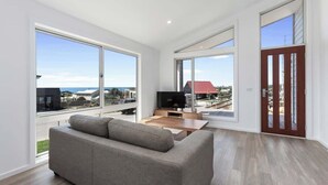 A modern living room with large windows, a sofa, a TV, and a wooden coffee table. - Apollo Bay Getaway (Apollo Bay)