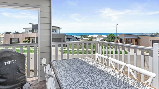 A balcony with a table and chairs, a grill, and a view of the ocean and neighboring buildings. - Apollo Bay Getaway (Apollo Bay)