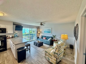 A modern kitchen with a built-in oven, a dining area with a table and chairs, a sofa, and a decorative chair with beach-themed upholstery.