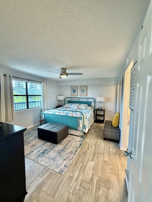 A bedroom with a bed, a ceiling fan, a window, a desk, and a door.