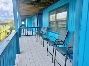 A covered porch with blue walls and wooden flooring, featuring two tables and four chairs.