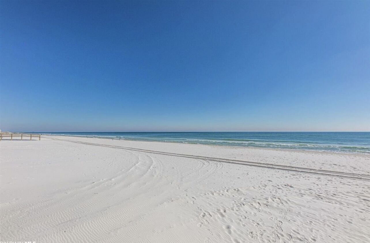 Une vaste plage de sable fin, sous un ciel bleu dégagé et une mer calme.