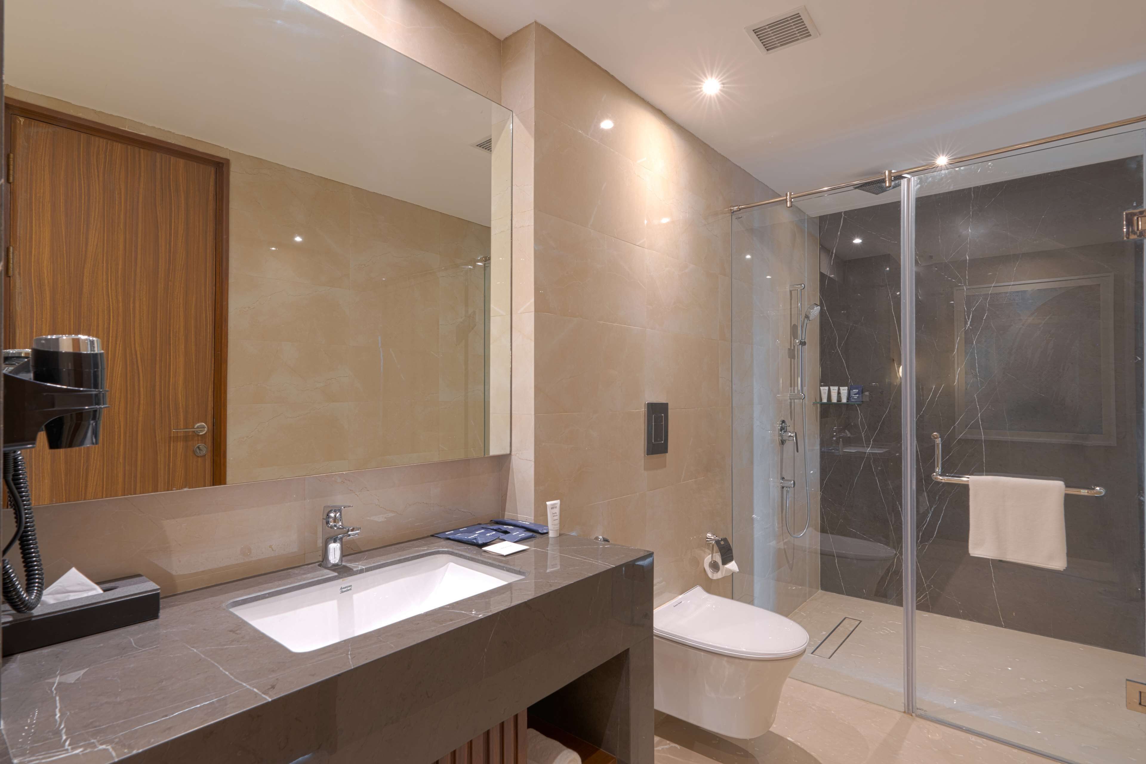 Un baño moderno con un espejo grande, un lavamanos, un inodoro y una zona de ducha con mampara de vidrio.
